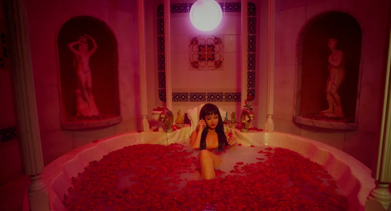 Helter Skelter (2012) movie still: medium — A lavish circular bathtub is filled with milk and scattered red rose petals. Two marble statues stand in…