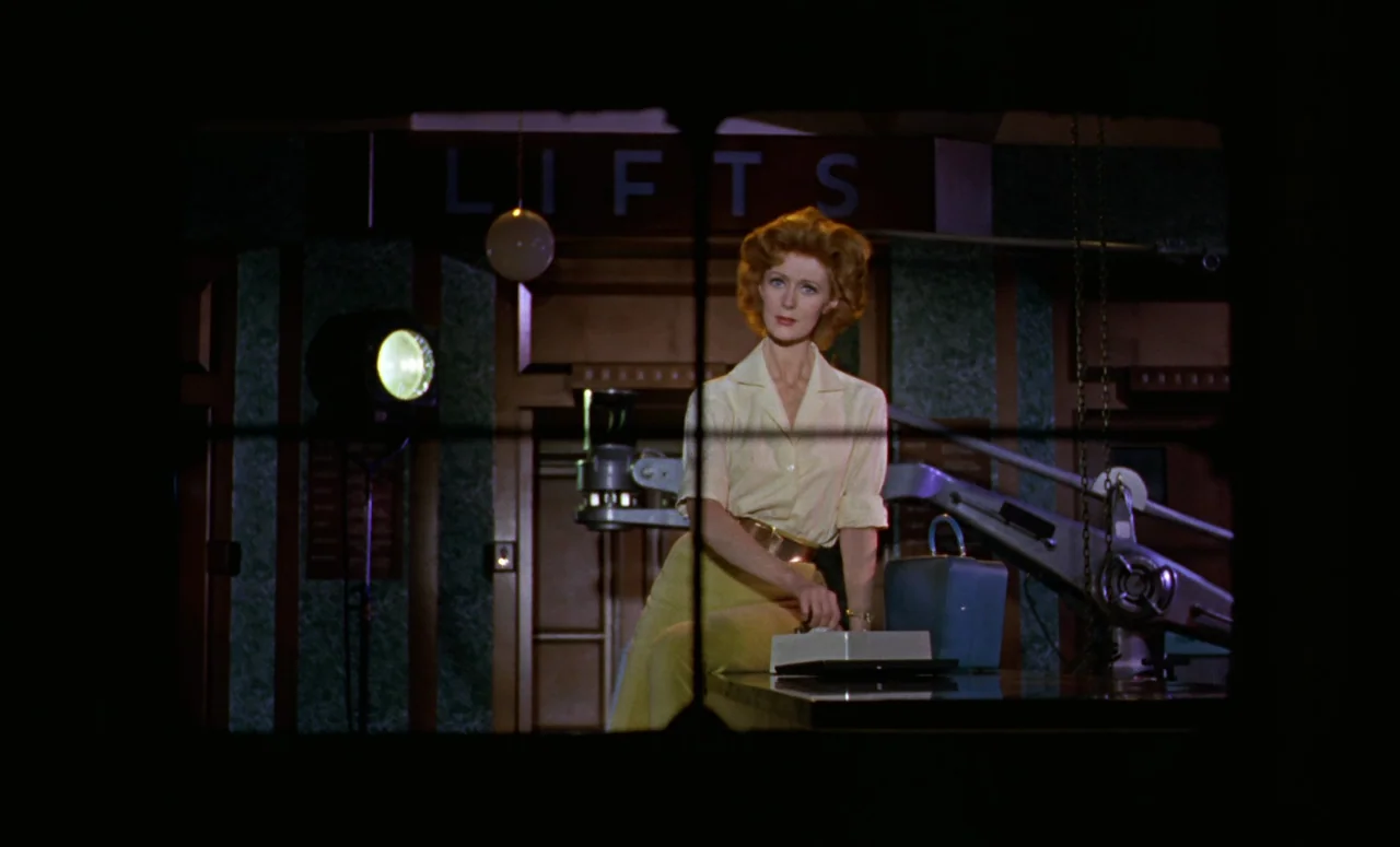 Peeping Tom (1960) movie still: medium — A dimly lit lobby features a sign reading LIFTS above a wooden paneled wall. A woman in a yellow blouse…