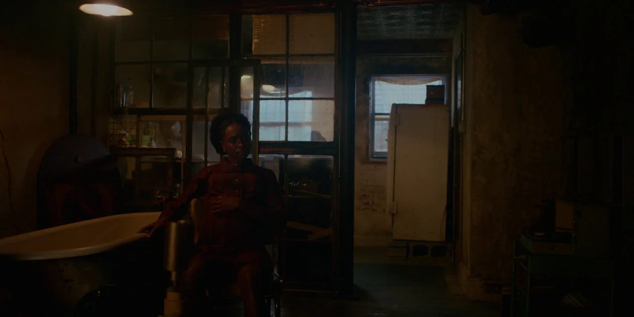 If Beale Street Could Talk (2018) movie still: medium — A dimly lit room features a white clawfoot tub and a large glass-paned partition. A woman…