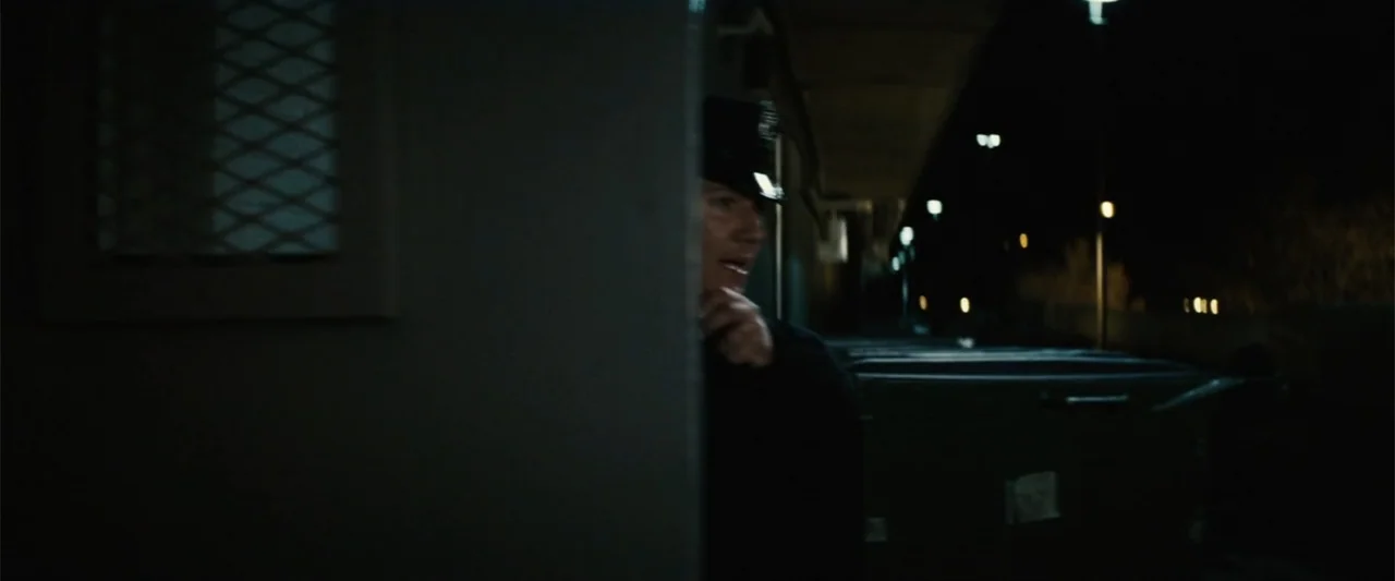 Run All Night (2015) movie still: medium — A dark concrete loading dock at night features industrial dumpsters and a metal doorway. A male police…