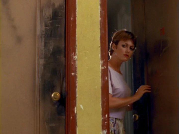 Tenement (1985) movie still: medium — A woman stands in a partially opened doorway of a room with yellow walls. She looks toward the side while…
