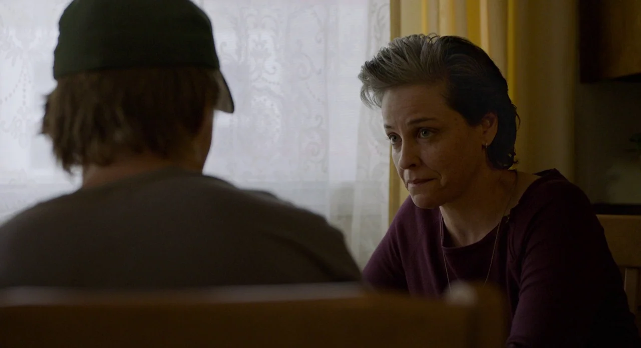 Lean on Pete (2017) movie still: medium — A quiet indoor setting features a person in a cap facing a middle-aged woman. The woman sits at a table…