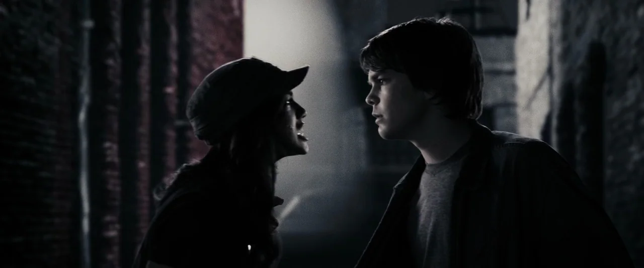 The Spirit (2008) movie still: medium — A narrow dark passage with textured brick walls on either side. A young woman faces a young man while…
