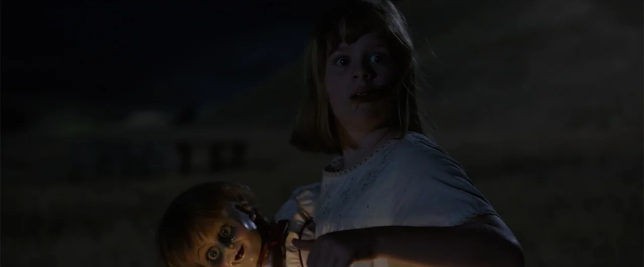 Annabelle: Creation (2017) movie still: medium — An open dark field at night surrounds a young girl and a doll. The girl holds the antique doll…
