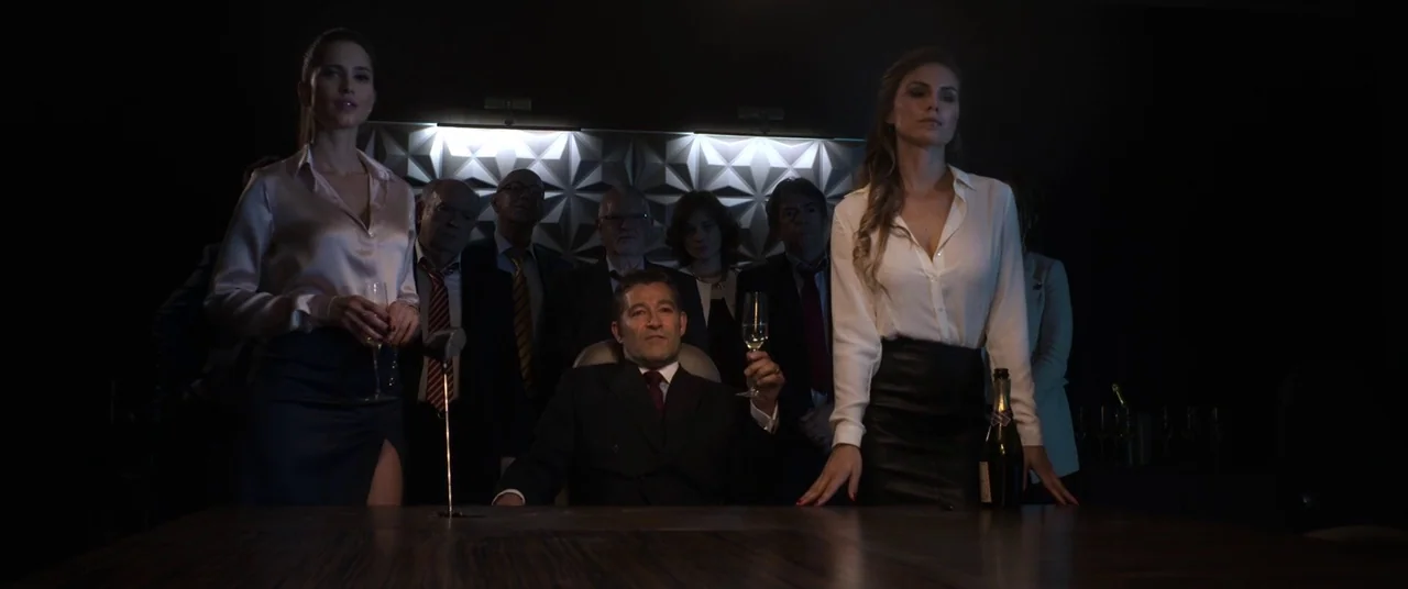 Mayhem (2017) movie still: medium — A dark boardroom with a textured white geometric wall backdrop and a large table. A man sits at the head of the…