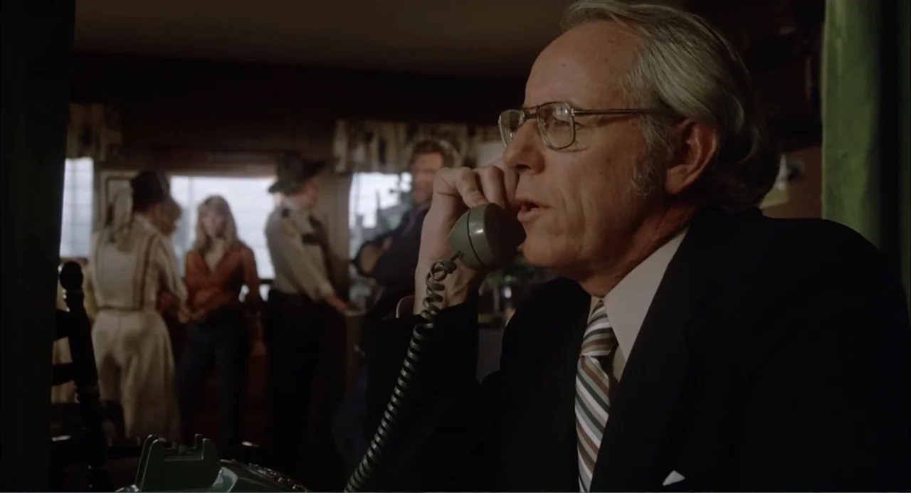 Empire of the Ants (1977) movie still: medium — A dimly lit professional office with wood-paneled walls and several people standing in back. An…