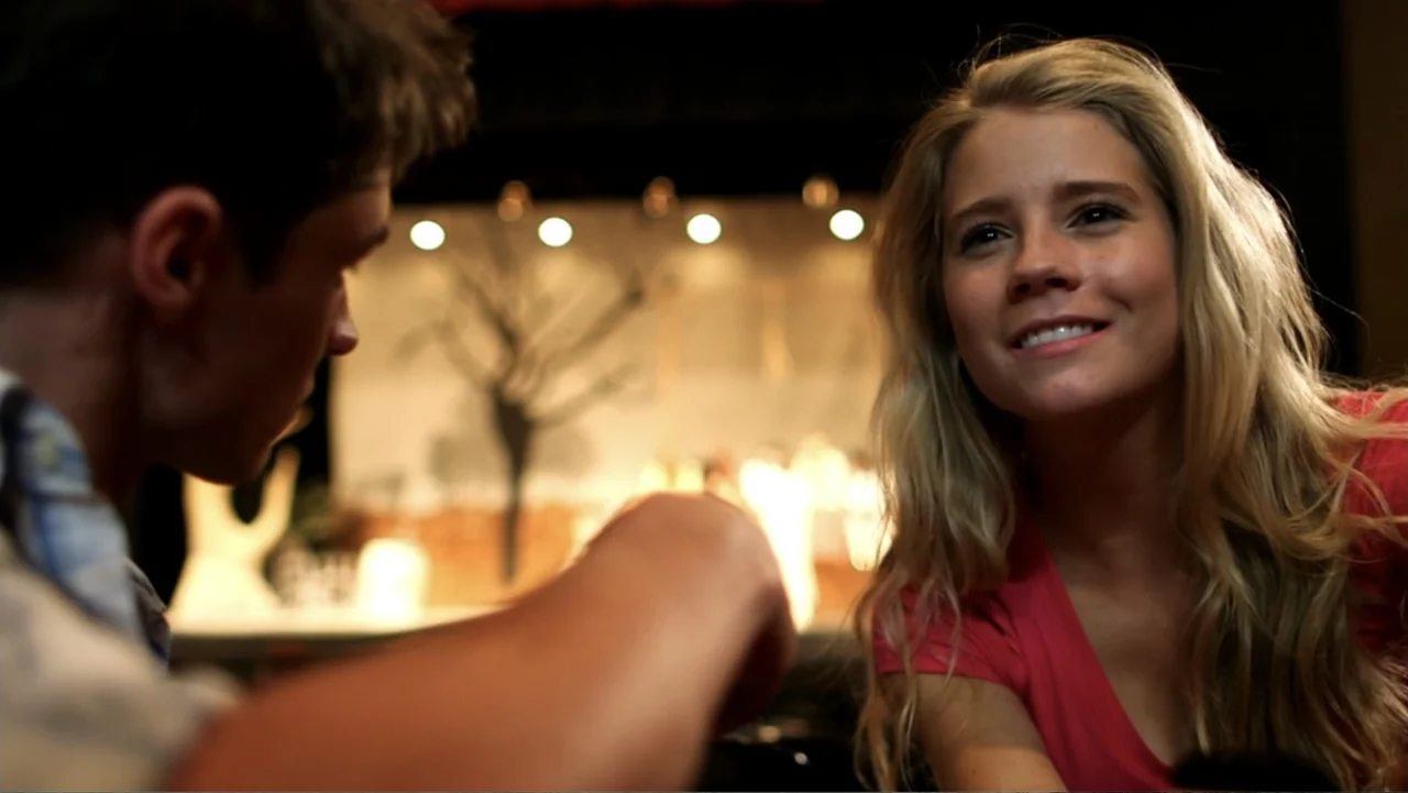 The Gallows (2015) movie still: medium — A dimly lit indoor dining space features a blurred background with soft circular lights. A young woman…