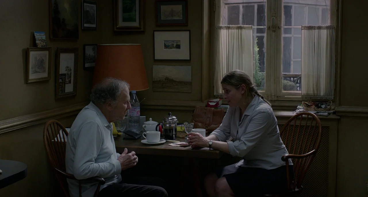 Amour (2012) movie still: medium — A small dining area features dark wooden furniture and walls adorned with numerous framed pictures. An elderly…