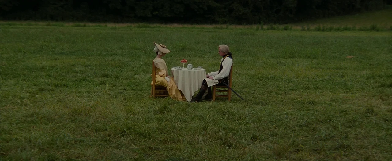 The Last of the Mohicans (1992) movie still: wide — A vast, open green field surrounds a small table set for tea. A man and a woman sit facing each…