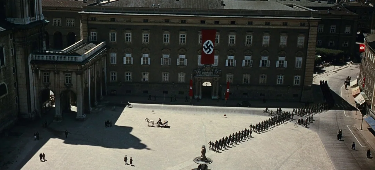 The Sound of Music (1965) movie still: establishing — A wide historic European square features large administrative buildings adorned with red Nazi…