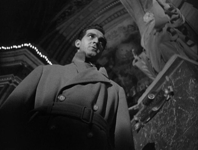 Mr. Arkadin (1955) movie still: medium — Inside a dimly lit stone cathedral, ornate architectural details loom in the shadows. A man wearing a heavy…