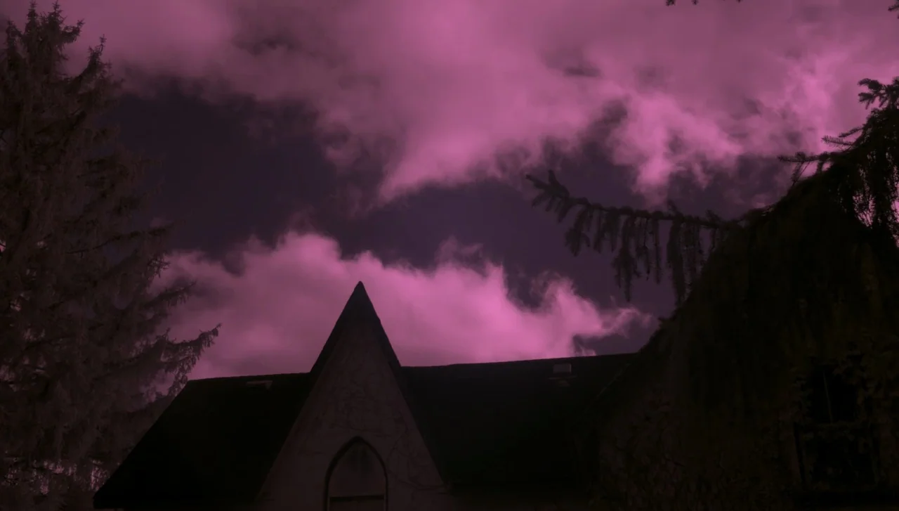Hellions (2015) movie still: wide — A dark house with a pointed gable roof stands against a magenta night sky. Dense clouds drift behind the…