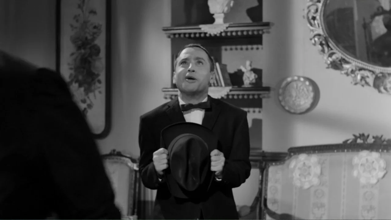 Escuela para solteras (1965) movie still: medium — A furnished interior space with ornate mirrors and shelves mounted on the wall. A man in a suit…