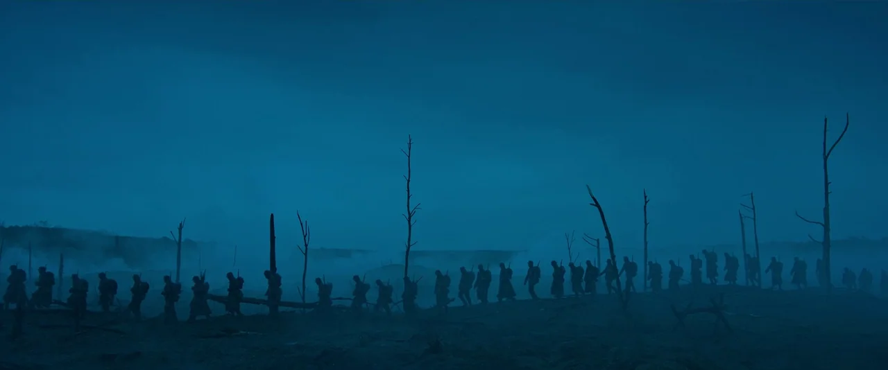 All Quiet on the Western Front (2022) movie still: wide — A desolate battlefield features bare, scorched trees under a thick, low-hanging mist. A…