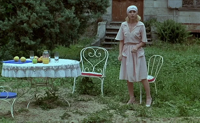 Maîtresse (1975) movie still: fullbody — A grassy garden with a round table covered in a white lace tablecloth. A blonde woman in a pink dress…