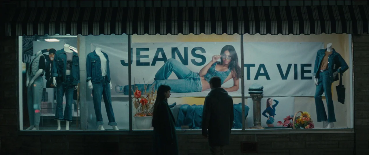 Humanist Vampire Seeking Consenting Suicidal Person (2023) movie still: wide — A nighttime storefront window features mannequins dressed in denim…