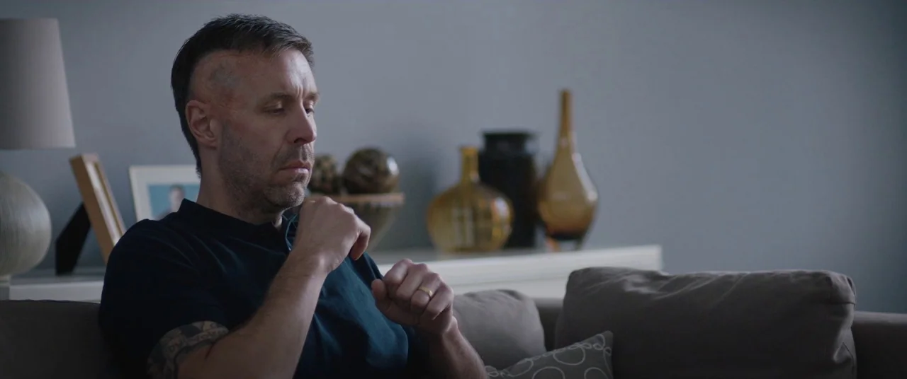 Journeyman (2017) movie still: medium — A quiet domestic space features a grey wall, a console table, and several glass vases. A middle-aged man…