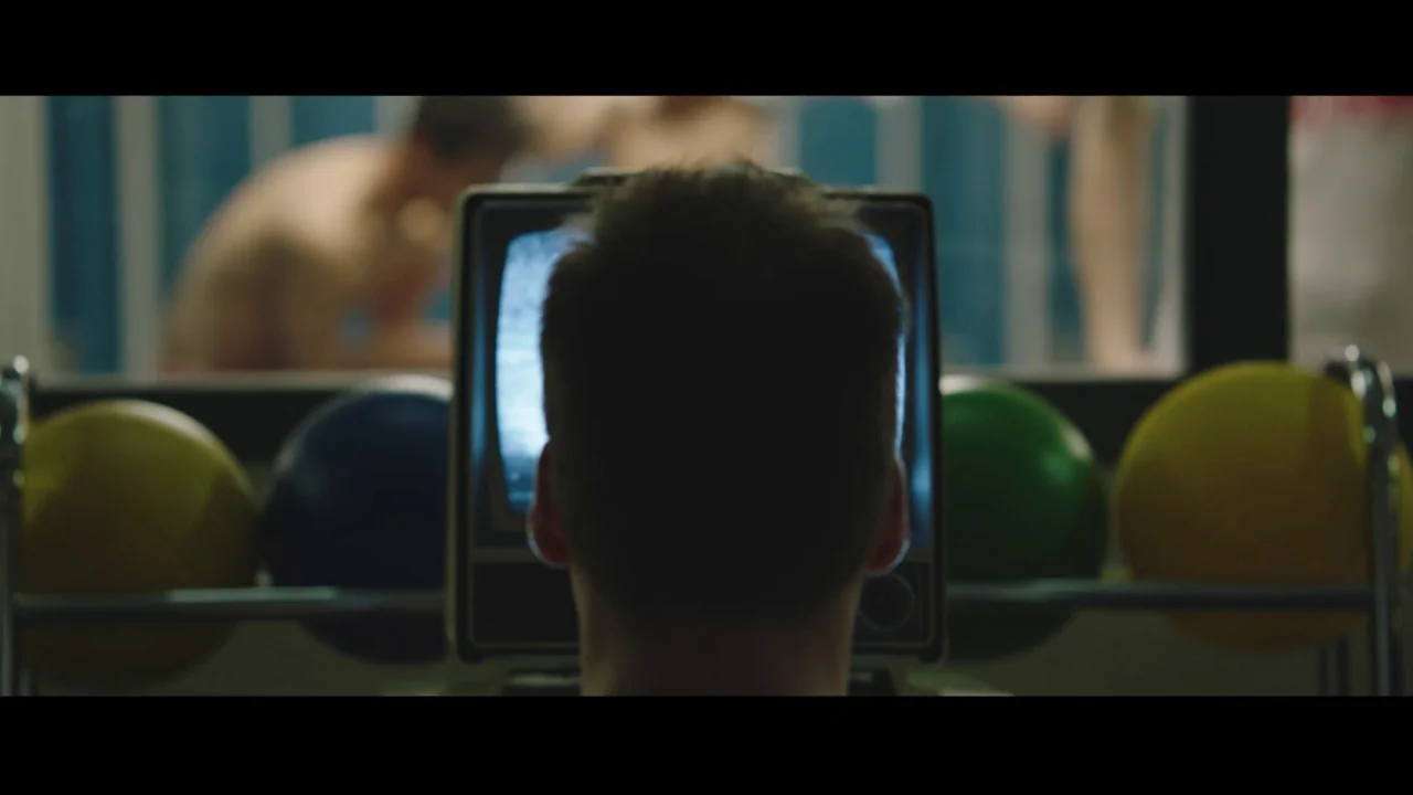 Collective: Unconscious (2016) movie still: medium — A man sits in front of a small portable television in a dim room. Rows of colorful bowling…