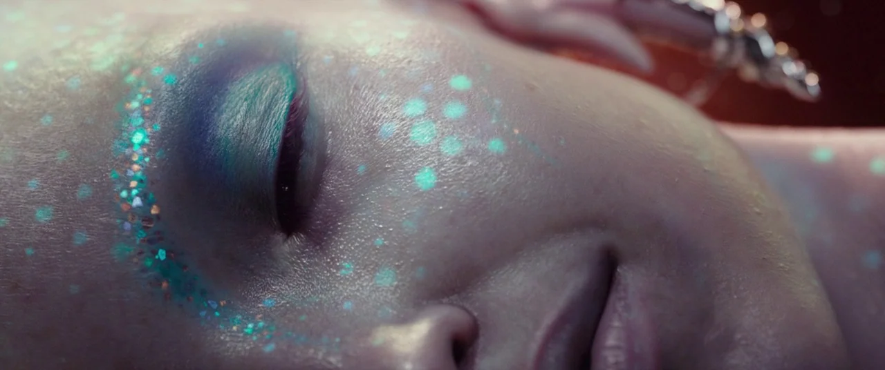 Valerian and the City of a Thousand Planets (2017) movie still: closeup — A close view of a person lying still in a dark environment. Teal glitter…
