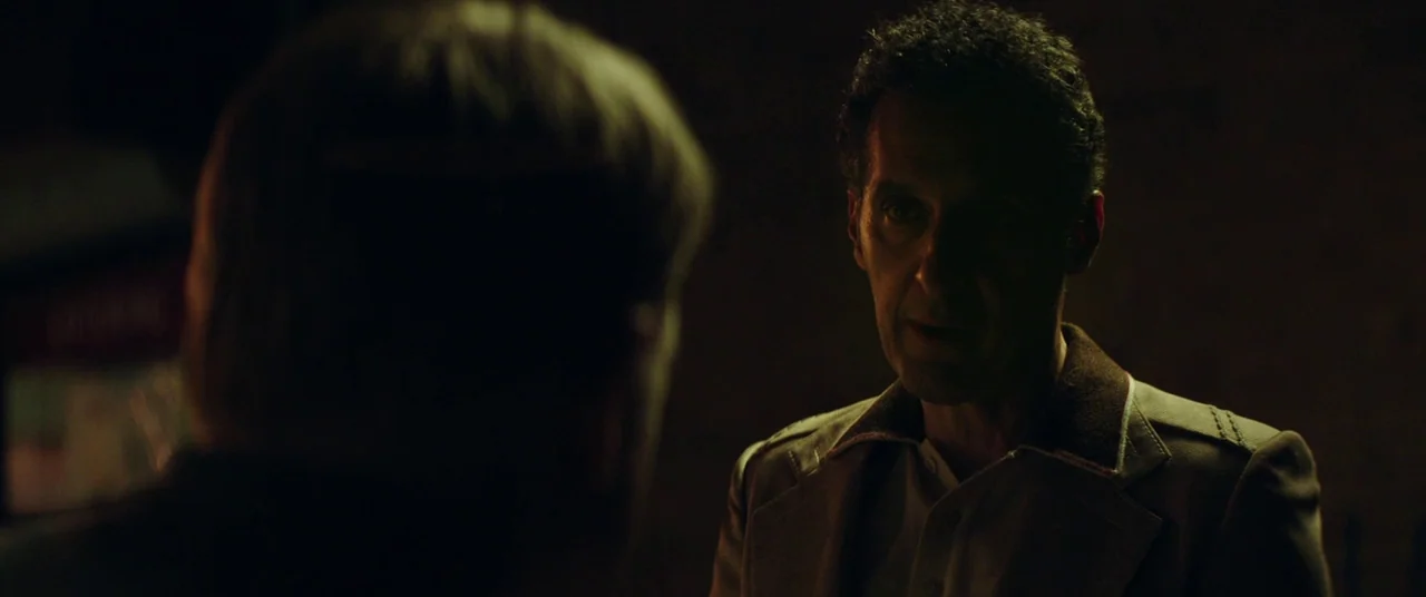 God’s Pocket (2014) movie still: medium — A man stands in a dark indoor space with minimal ambient light. He is captured in an over-the-shoulder…