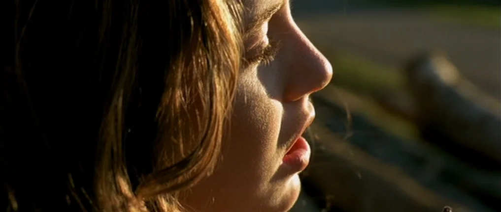 The Intruder (2004) movie still: closeup — A close-up side profile view captures a young woman outdoors during sunset. She has her eyes closed and…