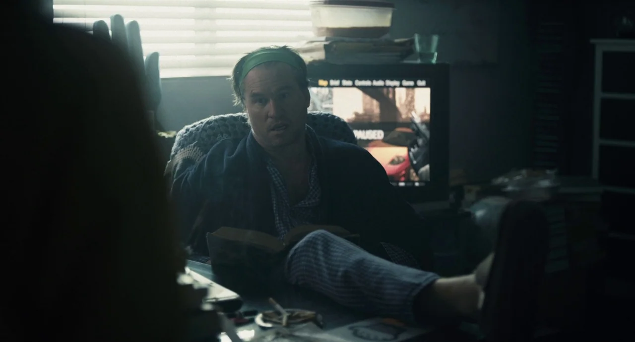 Palo Alto (2013) movie still: medium — A cluttered room with a television and window blinds in the background. A man reads a book at a desk with his…