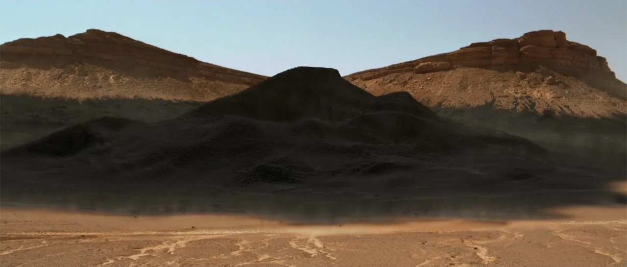 The Mummy Returns (2001) movie still: wide — A vast, arid desert landscape features a prominent, dark rocky mound in the center. The surrounding…