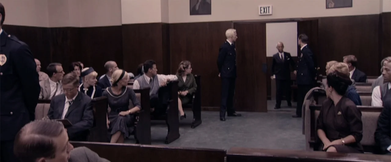 Dancer in the Dark (2000) movie still: wide — A courtroom interior features rows of wooden benches and dark wood-paneled walls. Several people…