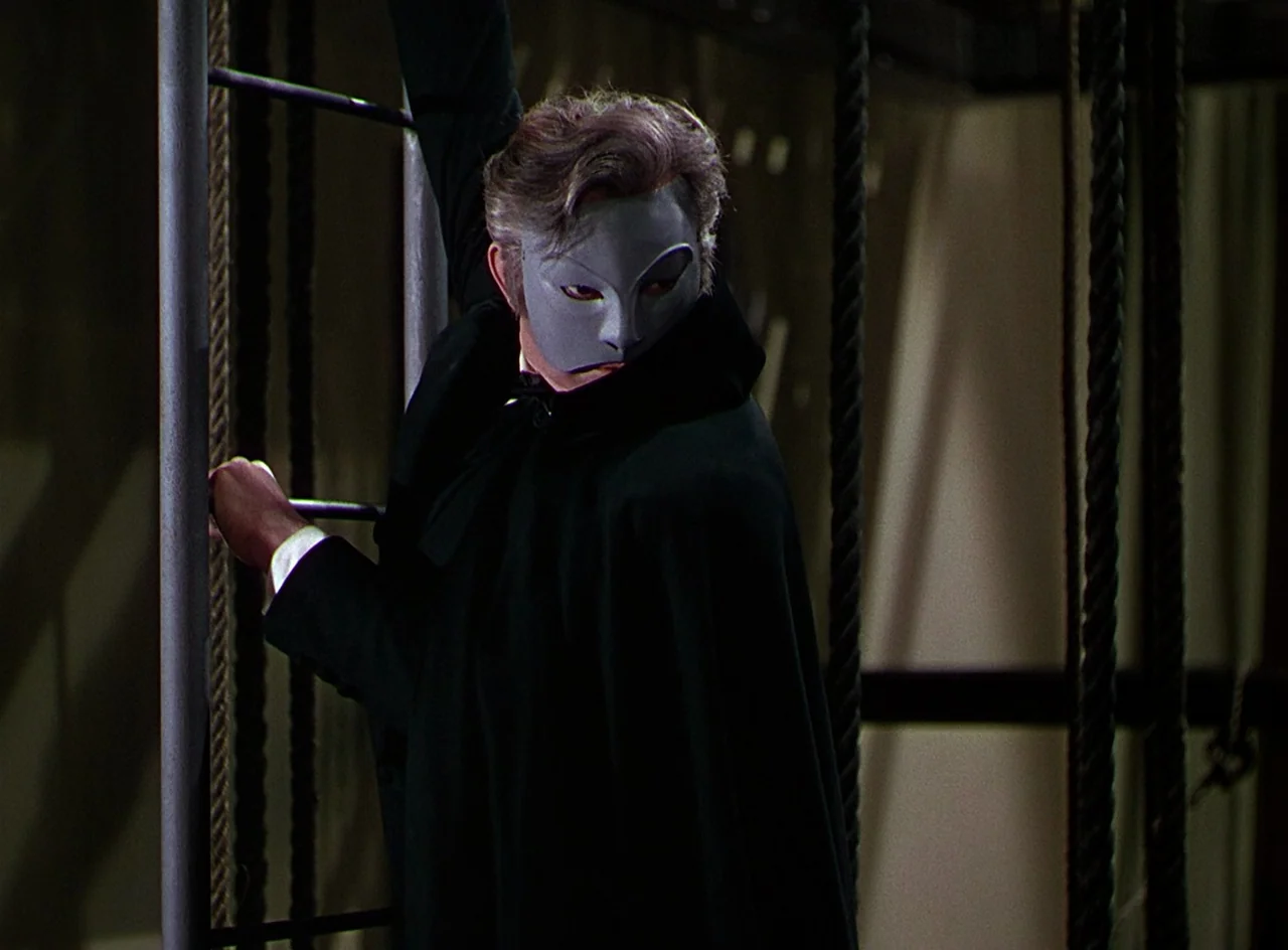 Phantom of the Opera (1943) movie still: medium — A high-contrast dark space featuring vertical steel poles and rigging ropes. A man wearing a grey…