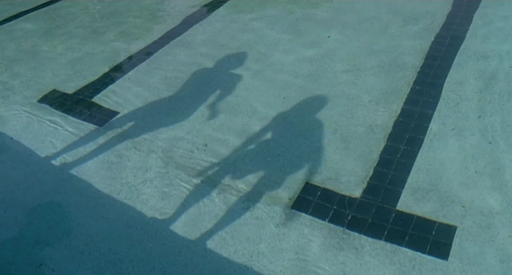 Y Tu Mamá También (2001) movie still: establishing — A view of the shallow end of a concrete swimming pool with black tile lane markers. Two…