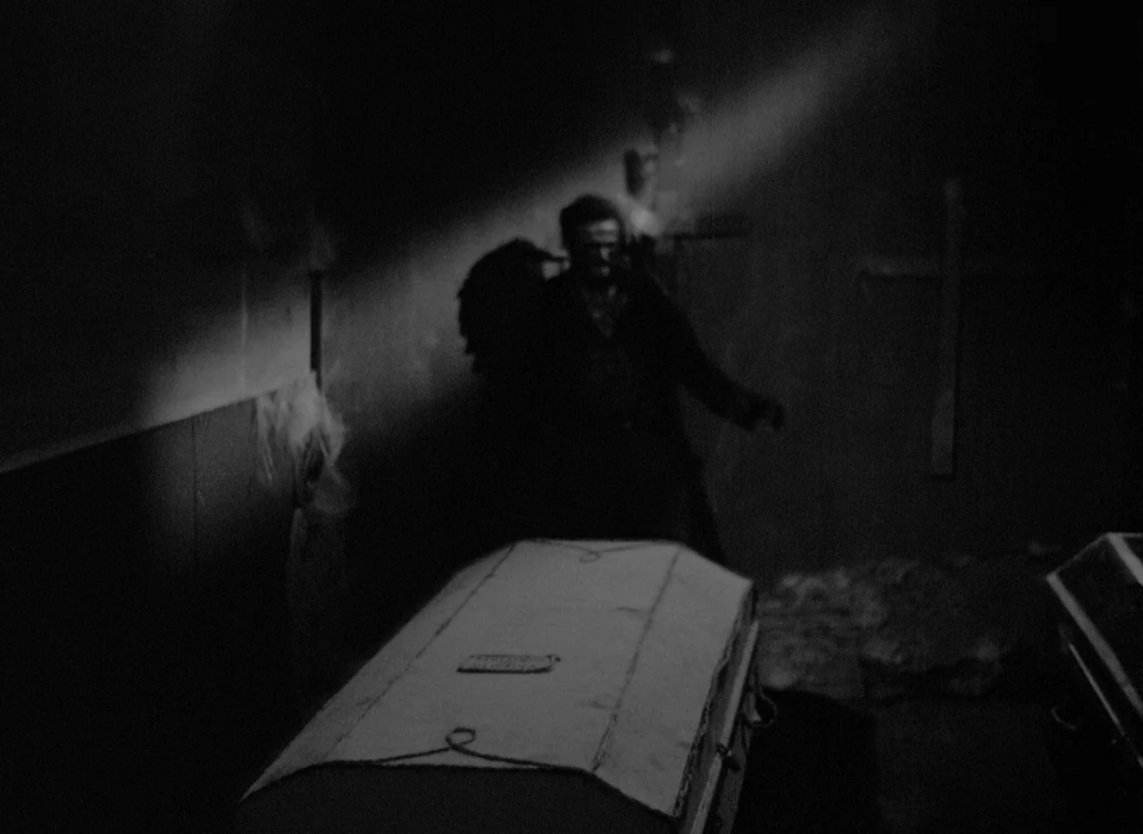 At Midnight I’ll Take Your Soul (1964) movie still: medium — A dimly lit stone interior features multiple coffins placed in a line. A man stands…