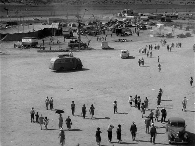 Ace In The Hole (1951) movie still: establishing — A vast, dusty open lot features a traveling carnival with tents and vehicles. Numerous…