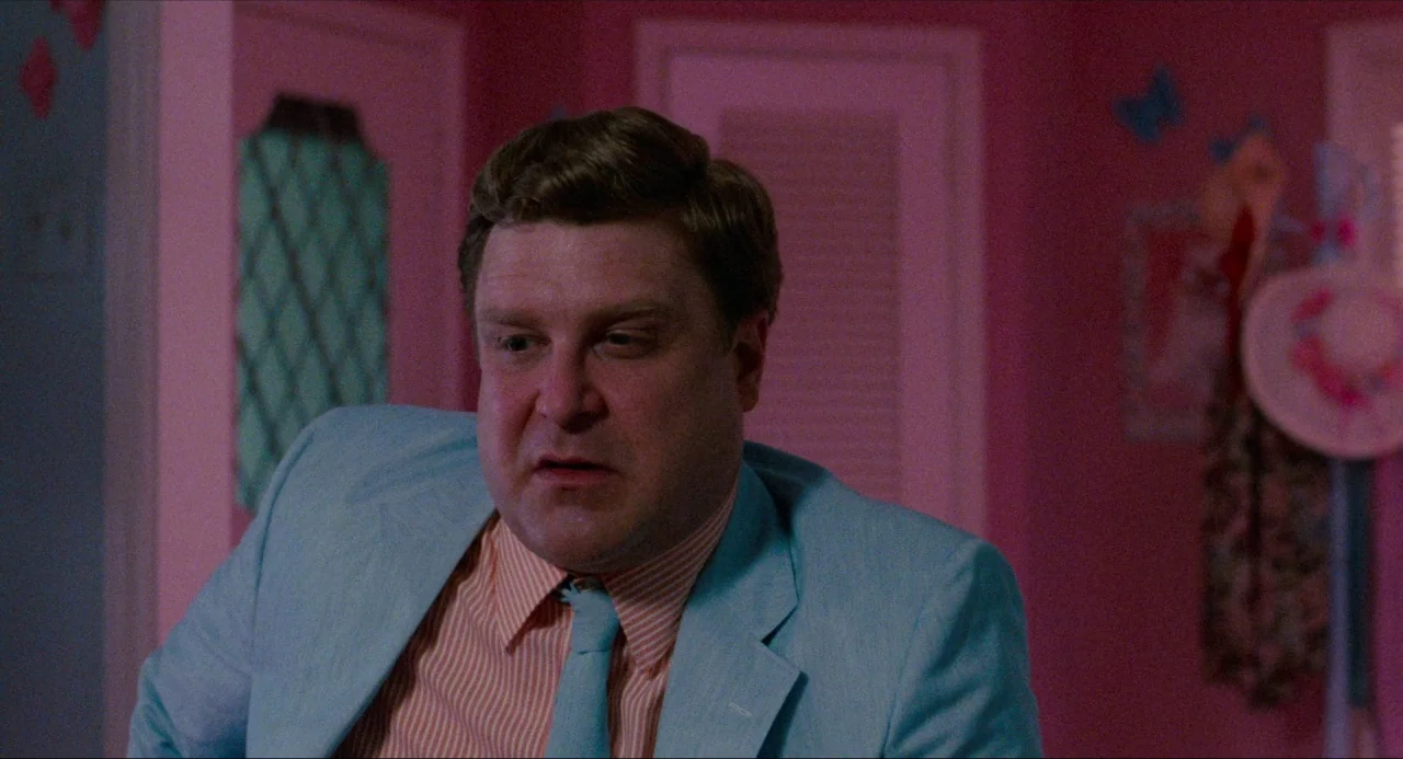 True Stories (1986) movie still: medium — A room with bright pink walls features decorative butterfly decals and a hanging sun hat. A man in a blue…