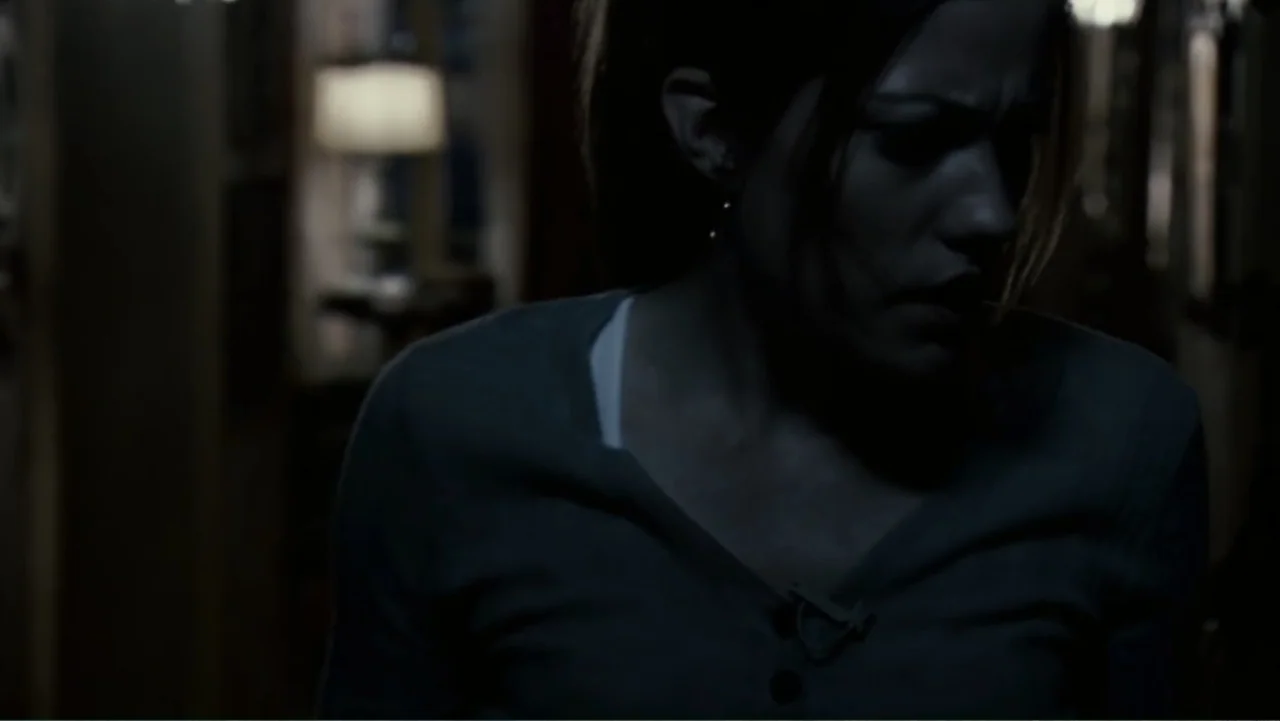 Quarantine (2008) movie still: medium — A dimly lit residential hallway at night with a distant lamp glowing softly. A young woman in a dark shirt…