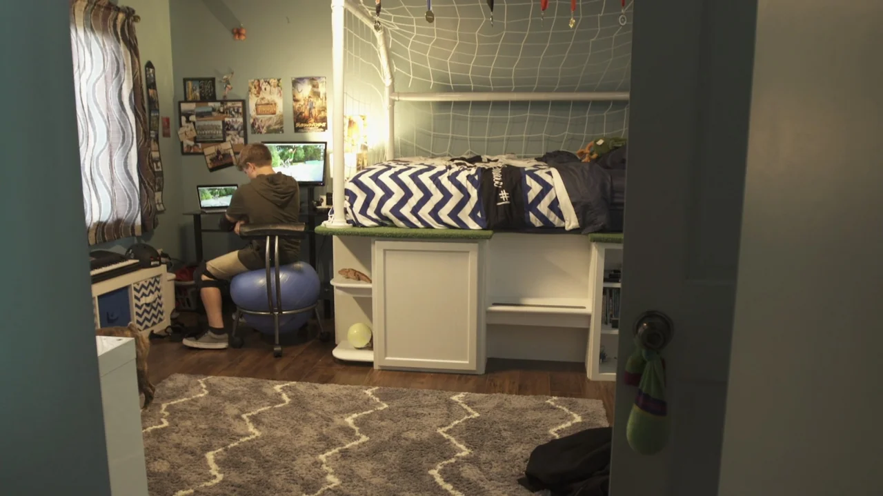 Sk8 Dawg (2018) movie still: medium — A teenager's room featuring a loft bed with a soccer net and computer desk. A boy sits on a blue exercise ball…