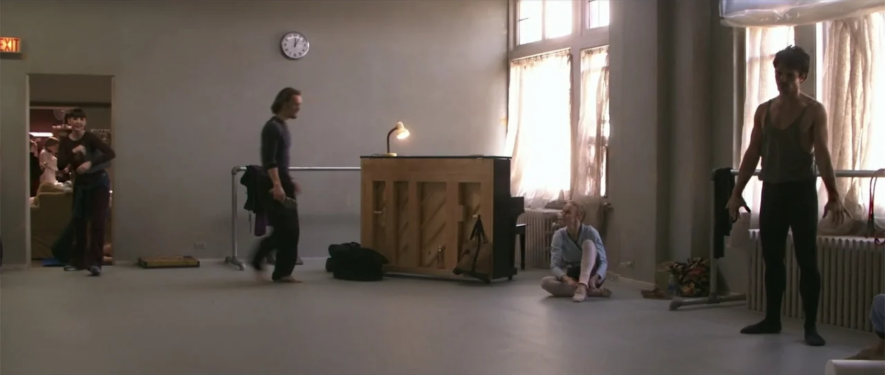 El acto (1989) movie still: wide — A spacious dance studio with a wooden upright piano and ballet bars. Dancers stand and sit on the floor while…