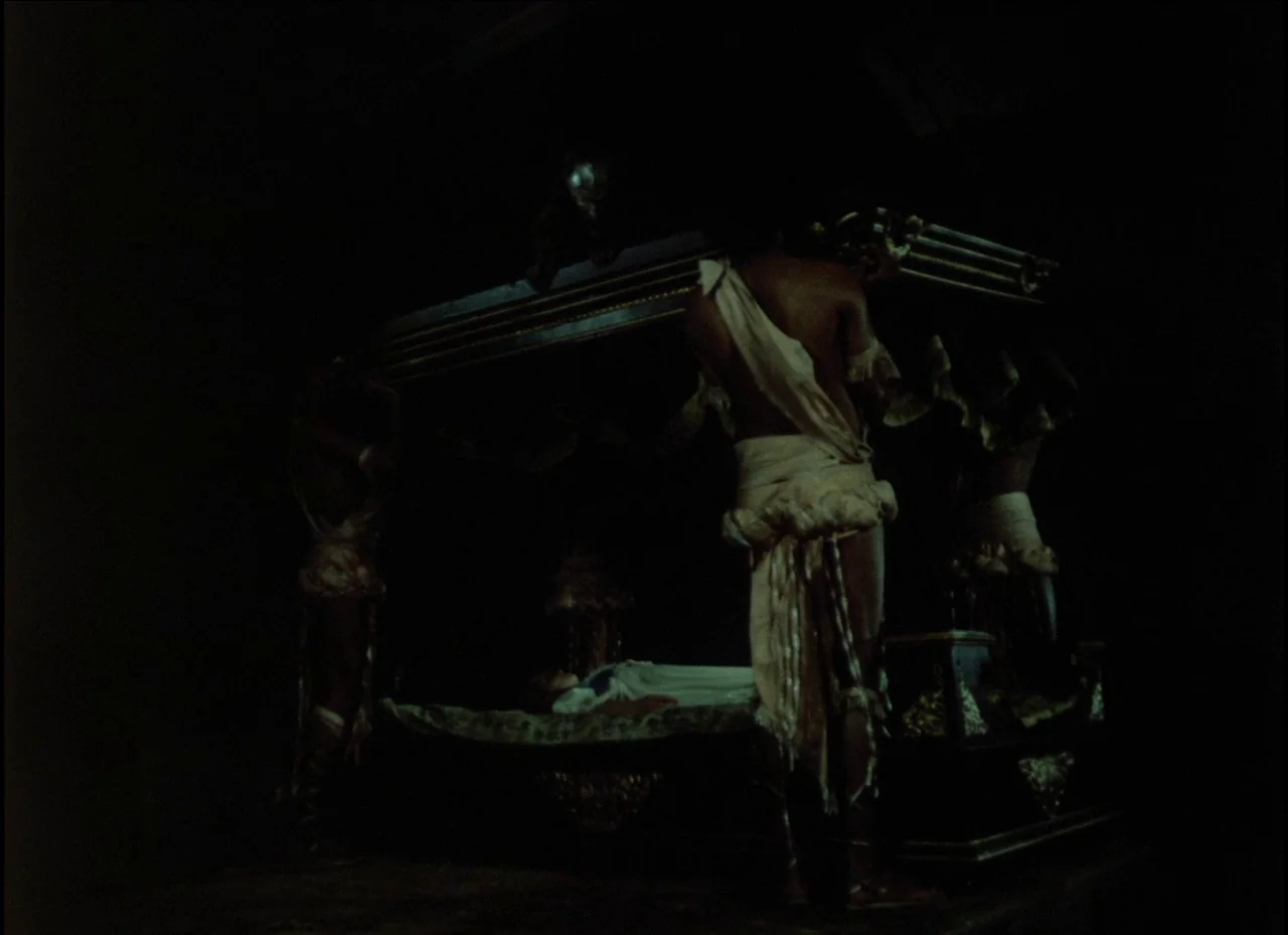 Beauty and the Beast (1979) movie still: medium — A dark, minimally lit space contains an ornate canopy bed as the central feature. A bare-chested…