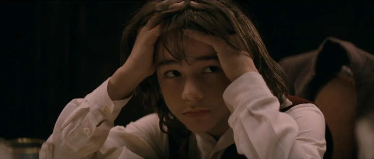 A Farewell to Fools (2013) movie still: closeup — A dimly lit interior space with shadows obscuring the background. A young person holds their head…
