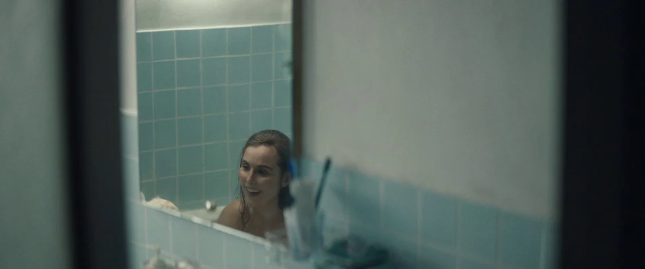 Babel (2006) movie still: medium — A bathroom features light blue tiled walls and a large rectangular vanity mirror. A young woman with damp hair is…