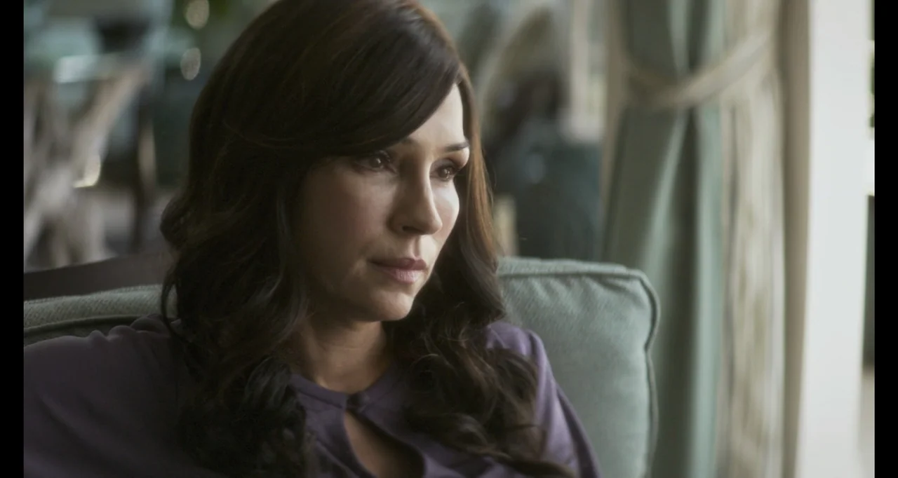 The Poison Rose (2019) movie still: closeup — A residential room featuring a soft-cushioned sofa and curtains visible in the background. A woman in…
