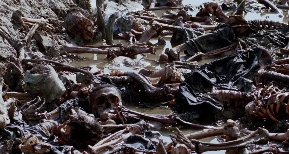 The Killing Fields (1984) movie still: establishing — A wet, muddy trench contains the remains of multiple decaying human skeletons. Black rags and…