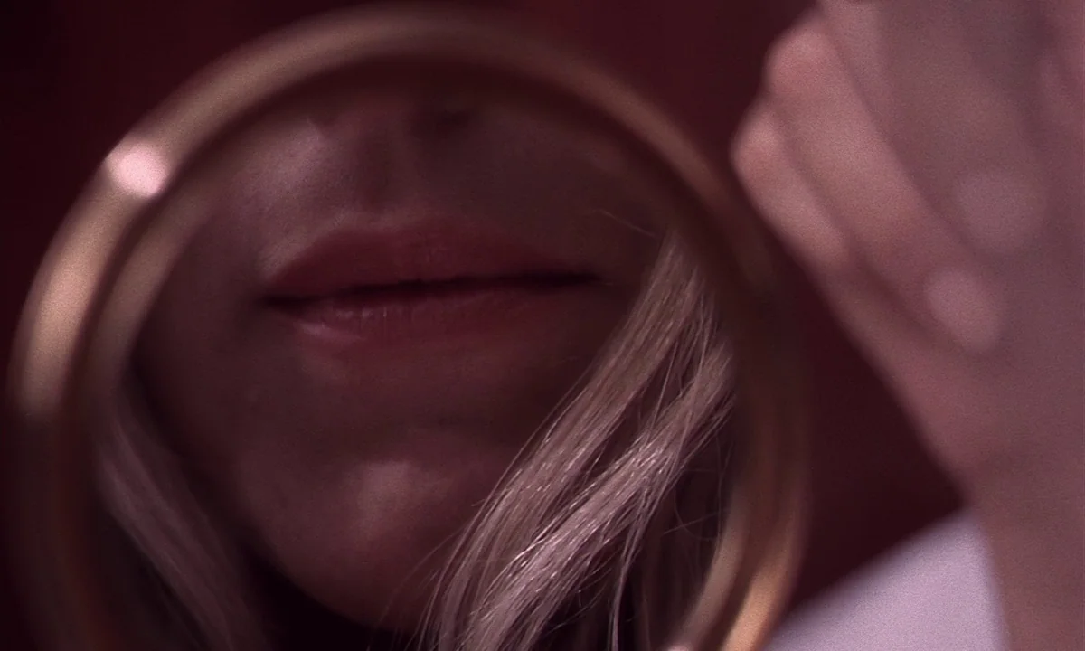 Daughters of Darkness (1971) movie still: closeup — A close-up view through a small circular hand mirror captures a woman's lower face. Her blonde…