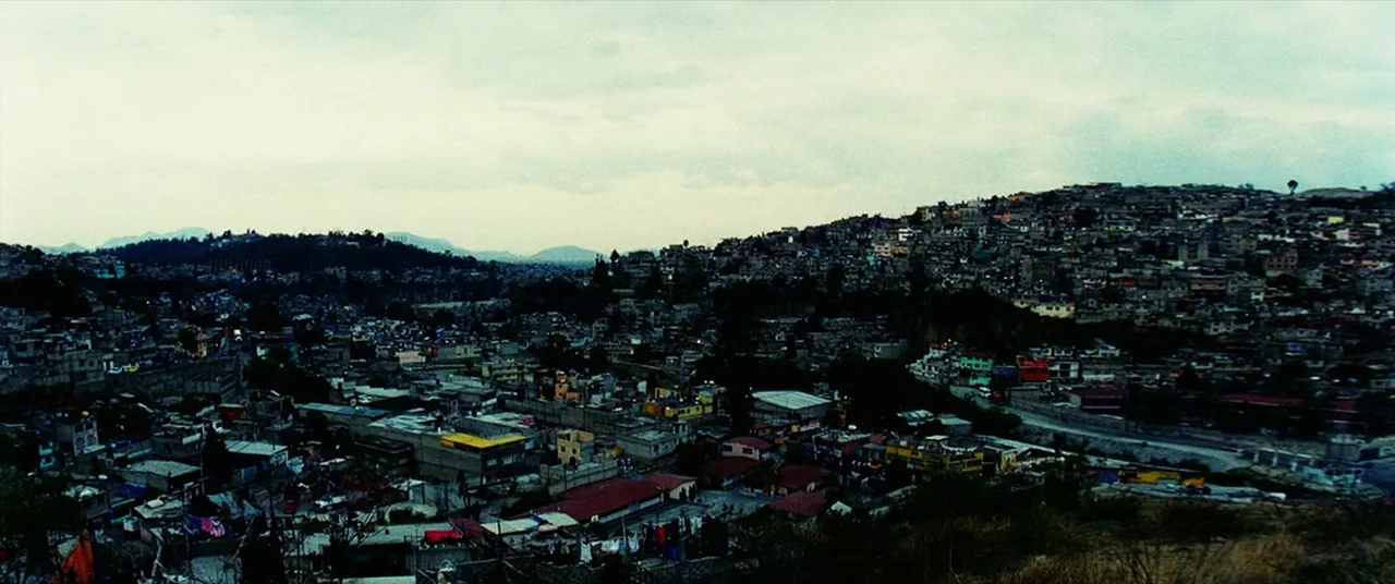 Man on Fire (2004) movie still: establishing — A dense hillside shantytown spreads across a valley under a thick overcast sky. Hundreds of small…