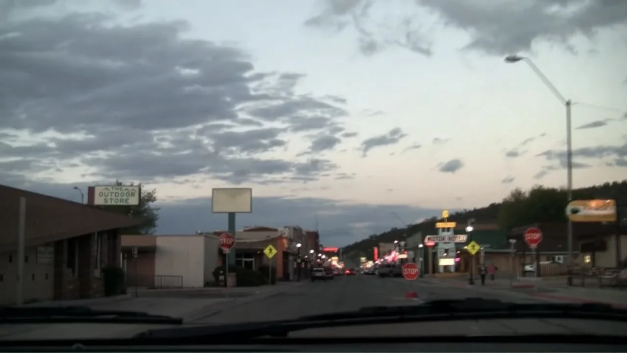 S-V/H/S: Un cortometraje de Las Crónicas del Miedo (2023) movie still: establishing — A small town main street at dusk with scattered shops and road…