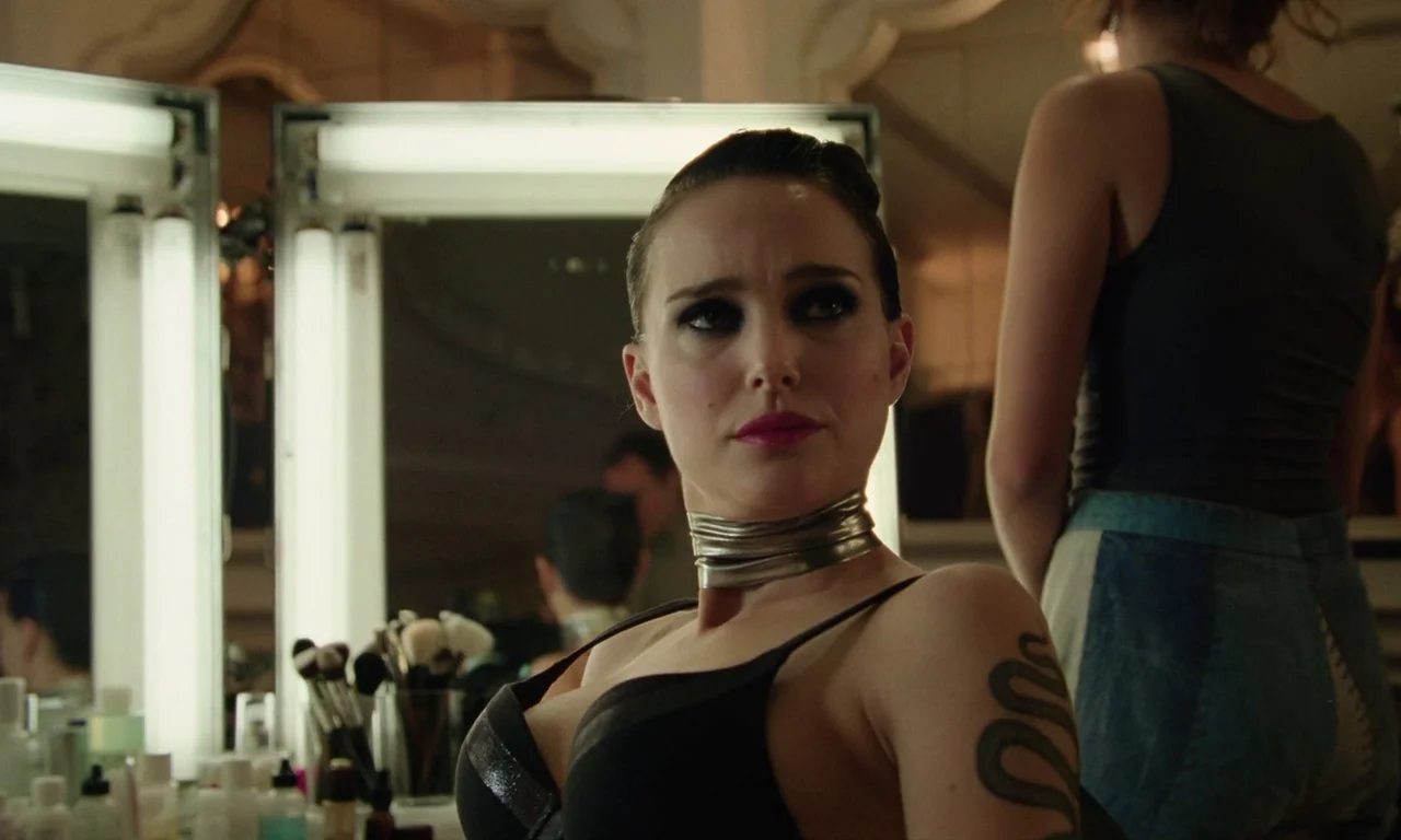 Vox Lux (2018) movie still: medium — A well-lit dressing room features a mirror surrounded by vertical fluorescent light tubes. A woman with a snake…
