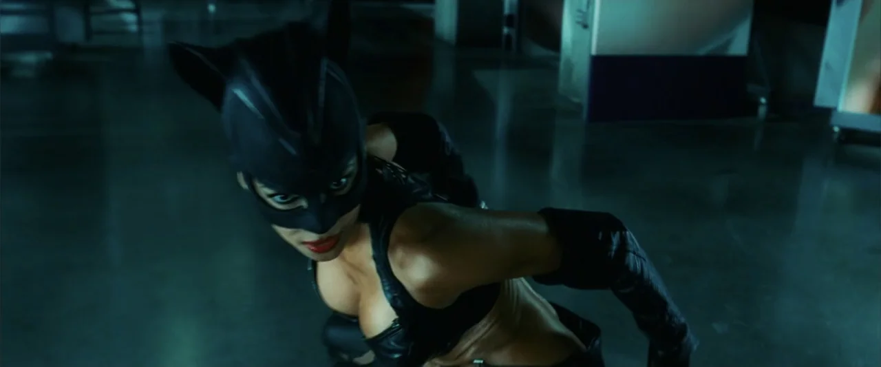 Catwoman (2004) movie still: medium — An interior industrial warehouse floor is bathed in dark teal tones. A woman in a black leather cat mask…