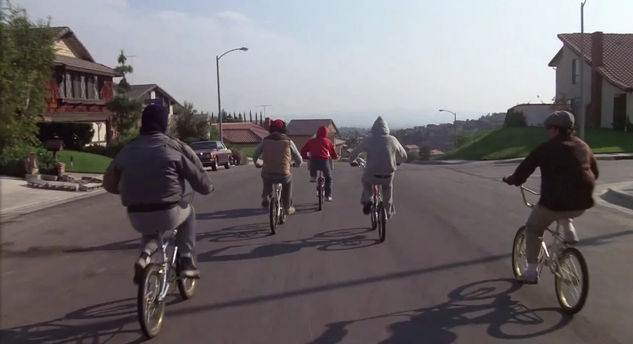 E.T. The Extra-Terrestrial (1982) movie still: wide — A quiet residential street lined with single-family houses during a clear afternoon. Five…