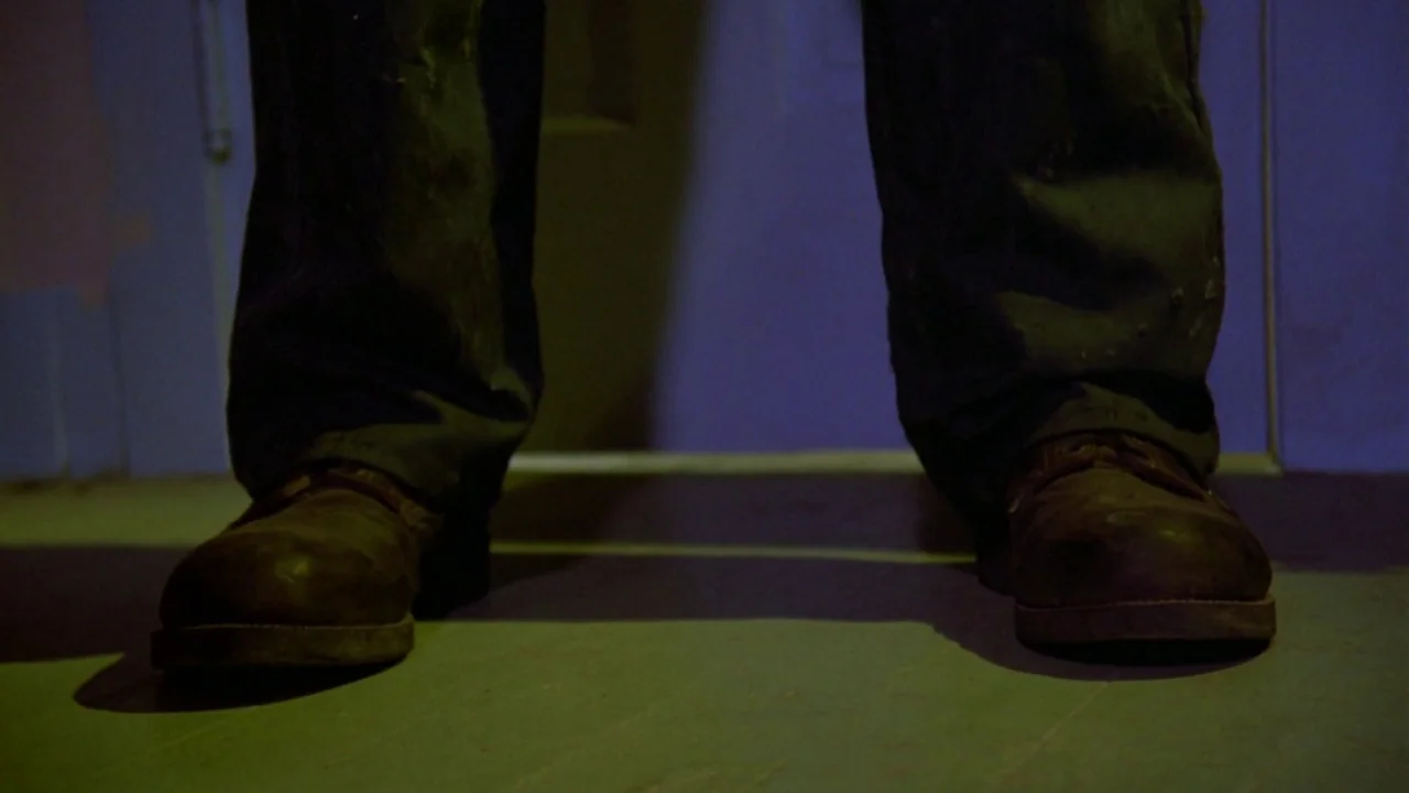 Friday the 13th: A New Beginning (1985) movie still: closeup — A close-up of a person's legs and boots standing on a dark wooden floor. The person…