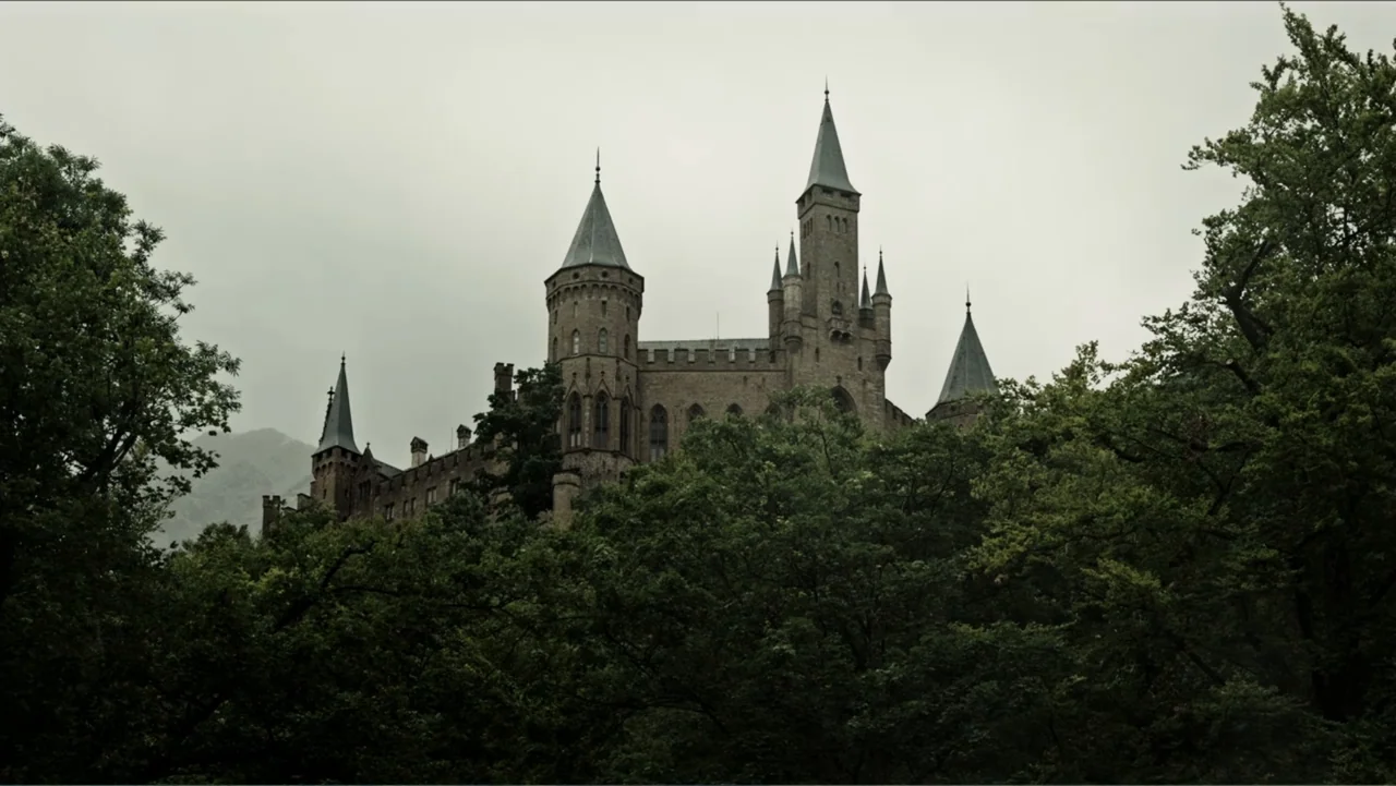 A Cure for Wellness (2017) movie still: establishing — A stone castle with multiple towers rises above a dense forest canopy. The structure sits…