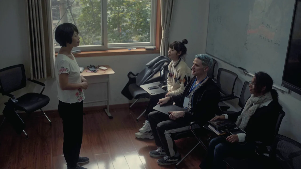 The Last Year of Darkness (2023) movie still: wide — A quiet classroom features a whiteboard with handwritten notes and chairs arranged in rows. A…